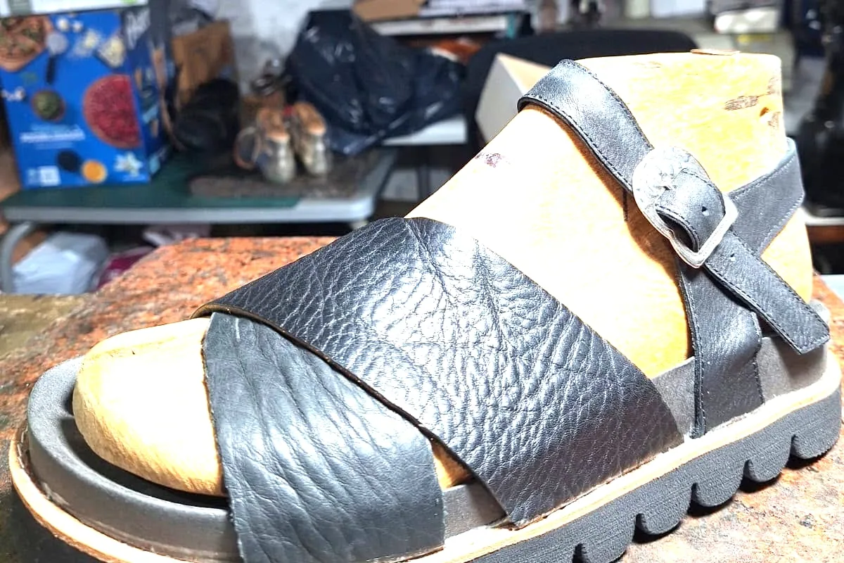 Sandalia negra de plataforma sobre la mesada, con las estanterías del taller detrás
