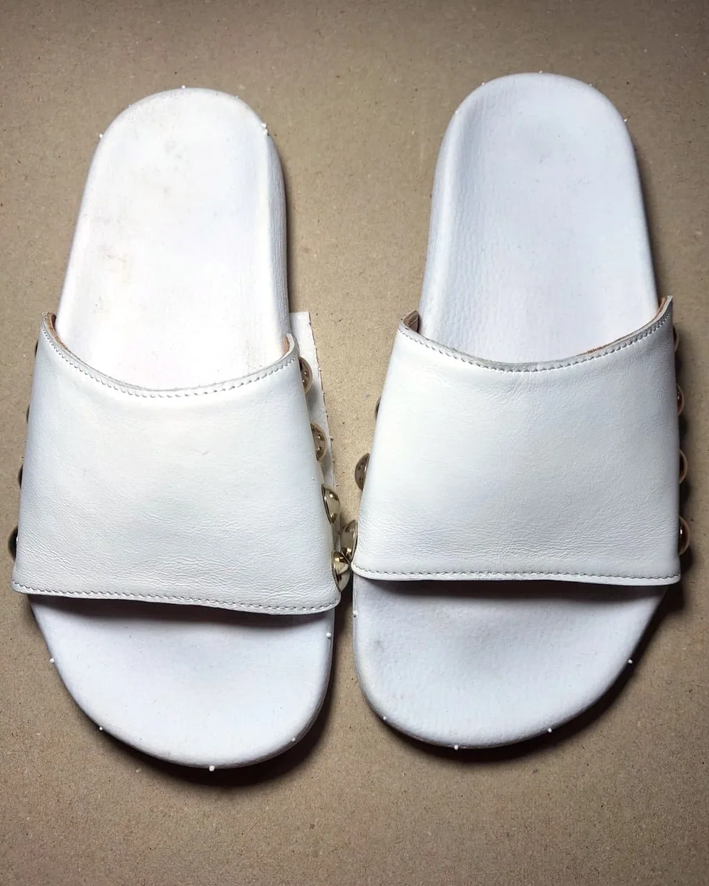Par de mules blancas de cuero, con tira ancha y tachas doradas a los costados