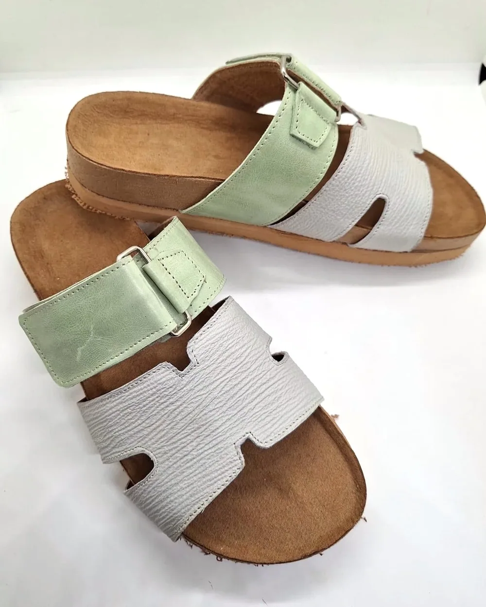 Par de sandalias verde agua y blanco, con tiras de cuero y hebilla sobre plantilla de corcho